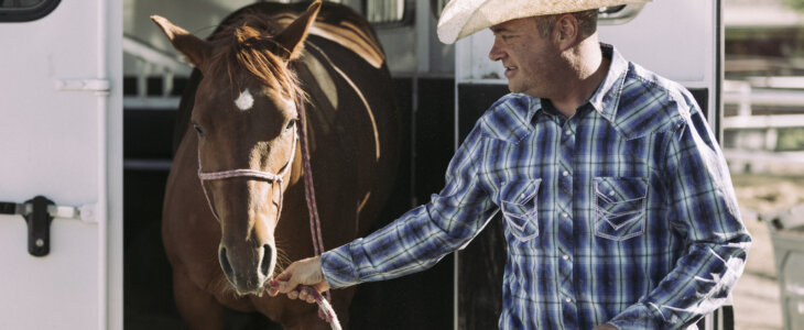 Man in a cowboy hat leading a brown horse out of a trailer